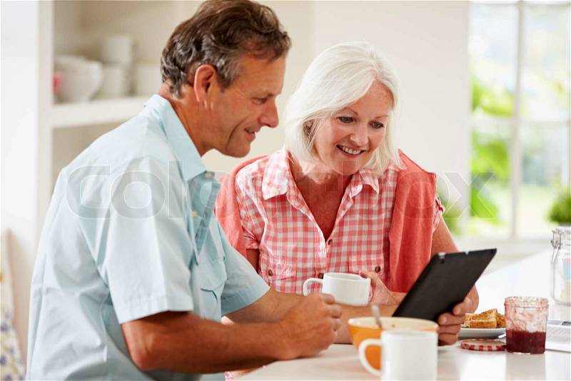 Middle Aged Couple Looking At Digital Tablet Over Breakfast, stock photo