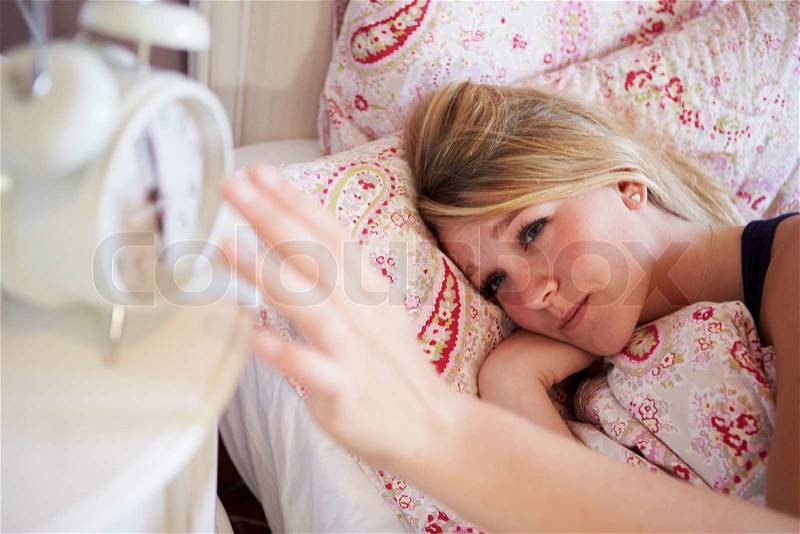 Teenage Girl Waking Up In Bed And Turning Off Alarm Clock, stock photo