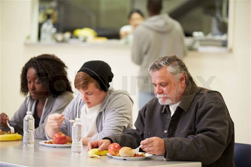 People Sitting At Table Eating Food In Homeless Shelter, stock photo