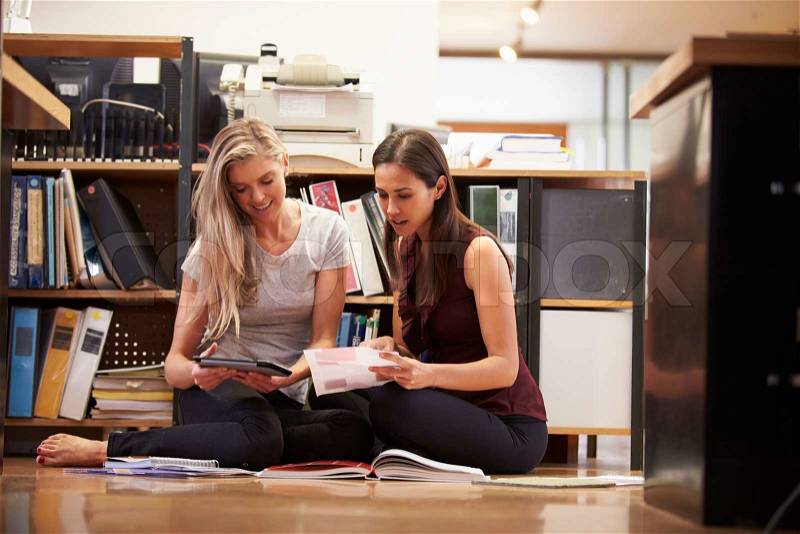 Two Businesswomen Sit On Office Floor With Digital Tablet, stock photo