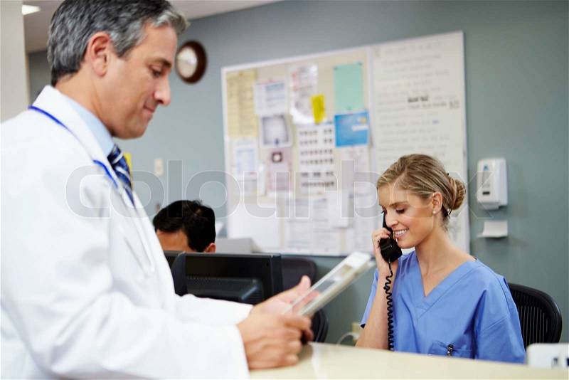 Doctor In Discussion With Nurse At Nurses Station, stock photo