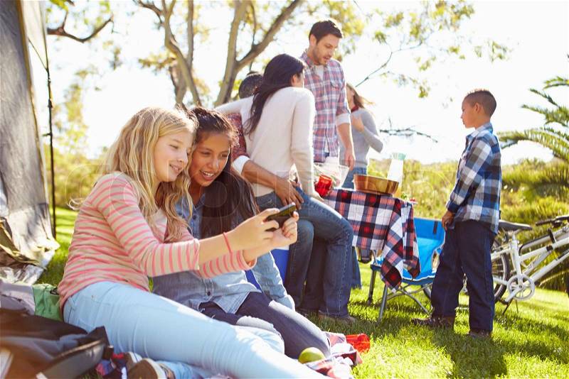 Two Girls Using Mobile Phone On Family Camping Holiday, stock photo