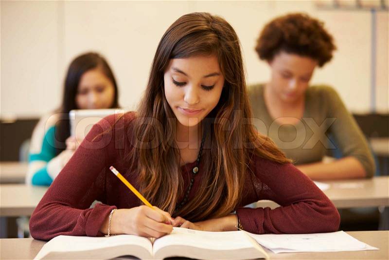 Female High School Student Studying At Desk In Classroom, stock photo