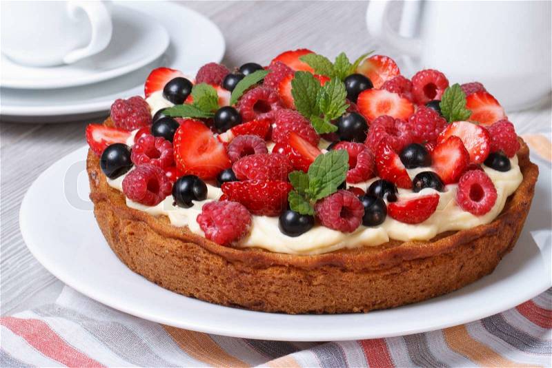 Fresh berry tart with strawberries, raspberries, currants, mint and cream close up on the table. horizontal , stock photo