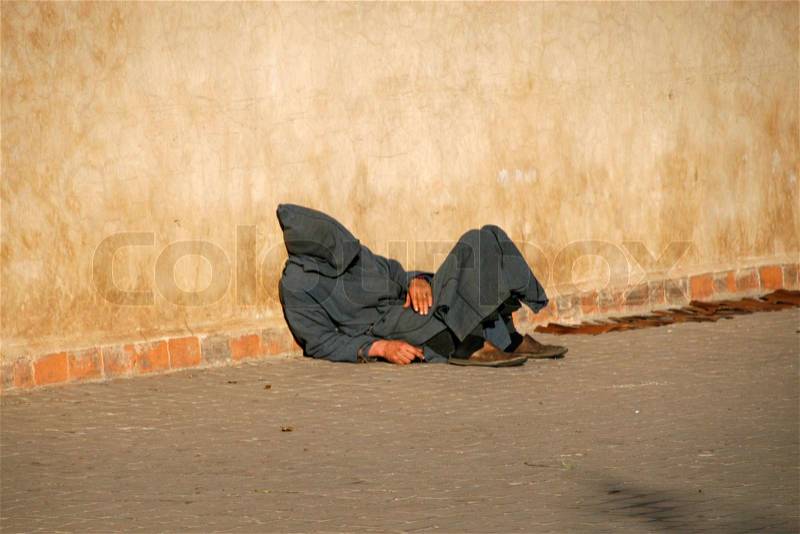 A arab guy is sleeping outside, near a wall, stock photo