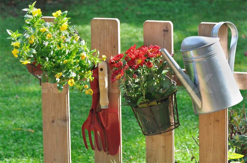 Flower pot, watering can and tools hanging on a fence in garden, stock photo