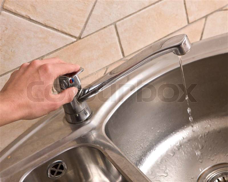 A hand holding the handle of a kitchen faucet, stock photo