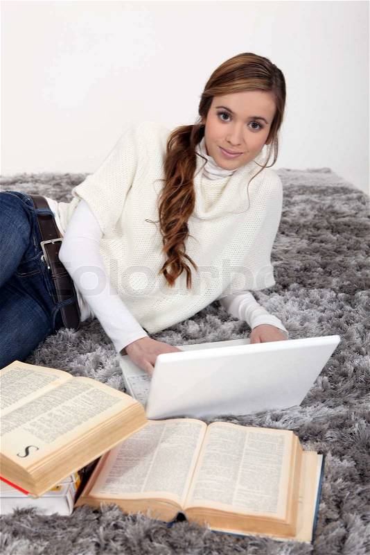 Woman laying on rug with laptop and books, stock photo