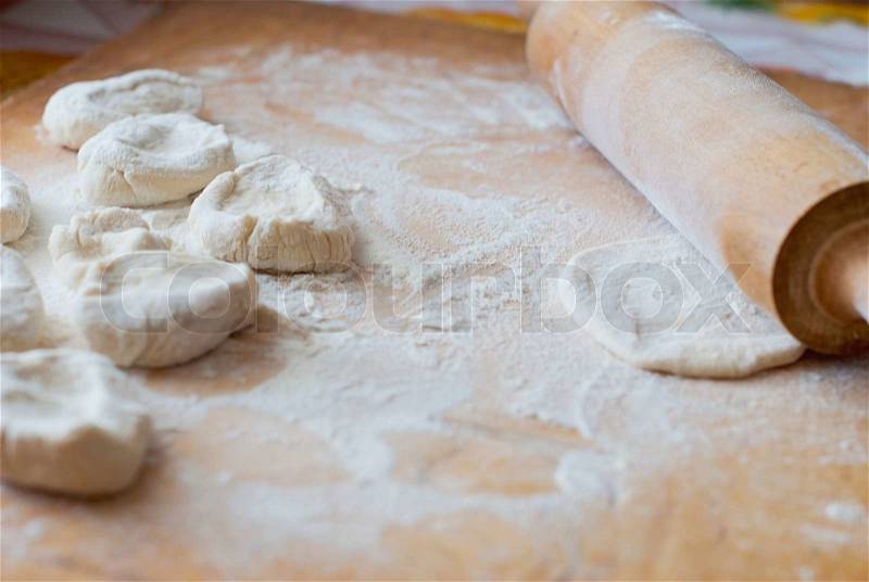 Small pieces of dough with flour on a wooden board with a rolling pin, stock photo