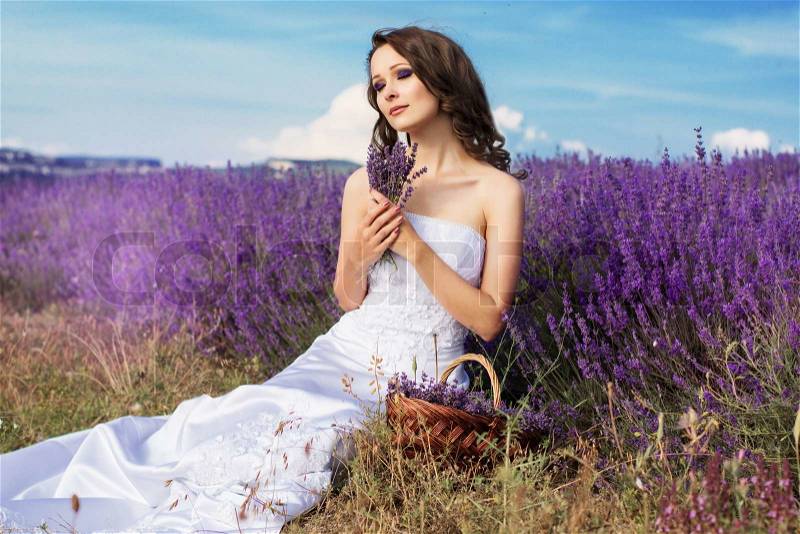 Beautiful bride posing at field of purple lavender with basket, stock photo