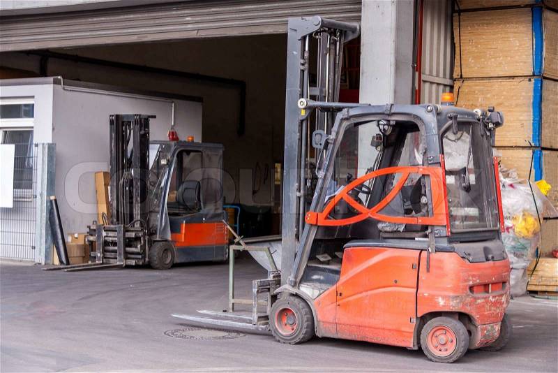 Small orange forklift parked at a warehouse used to move, raise stack and load wooden pallets for storage, distribution and delivery, stock photo