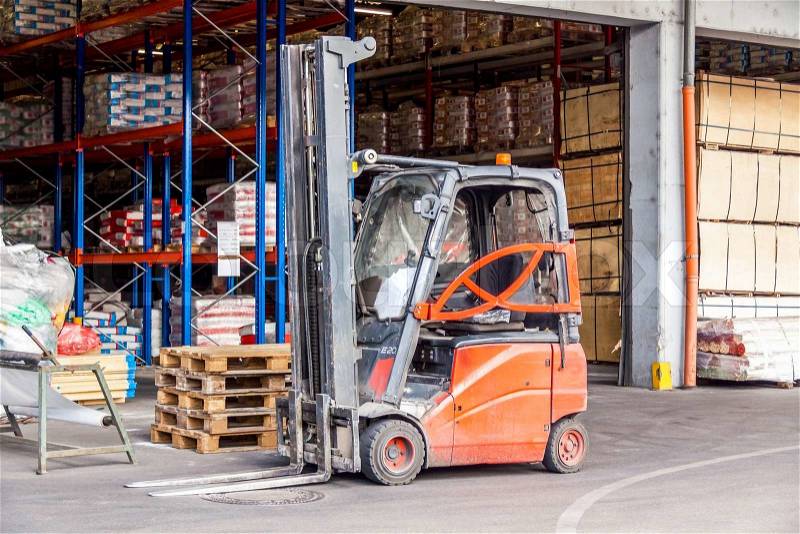 Small orange forklift parked at a warehouse used to move, raise stack and load wooden pallets for storage, distribution and delivery, stock photo