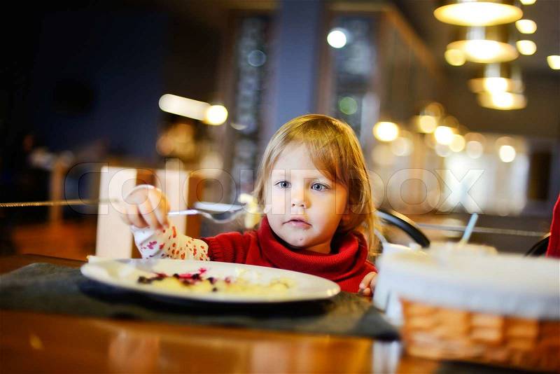 Toddler girl eating in restaurant, stock photo