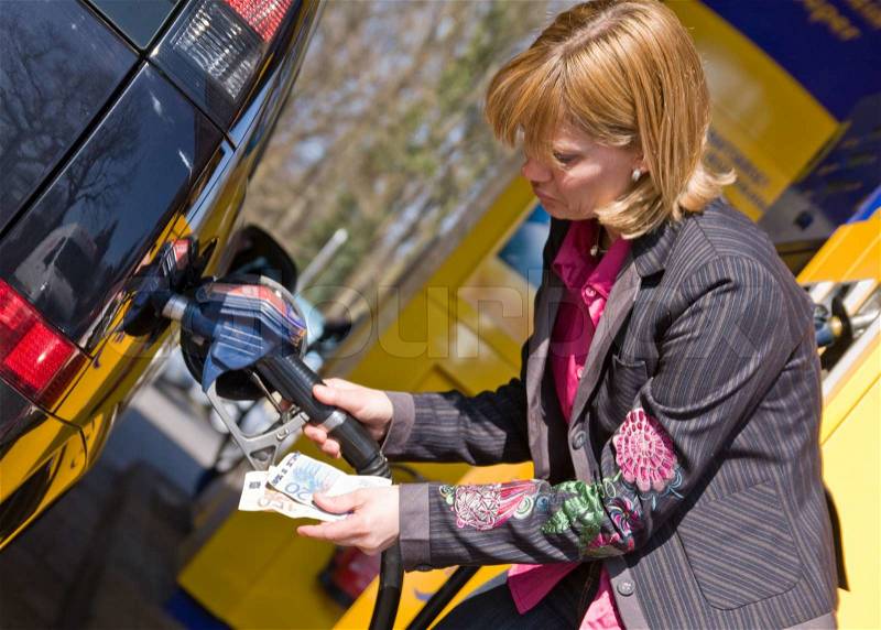 A woman holds cash while pumping gasoline in her car, stock photo