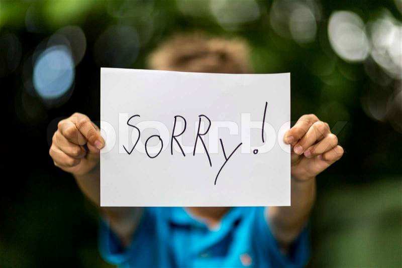 Blurred boy holding a piece of paper with the word Sorry in front of her, stock photo