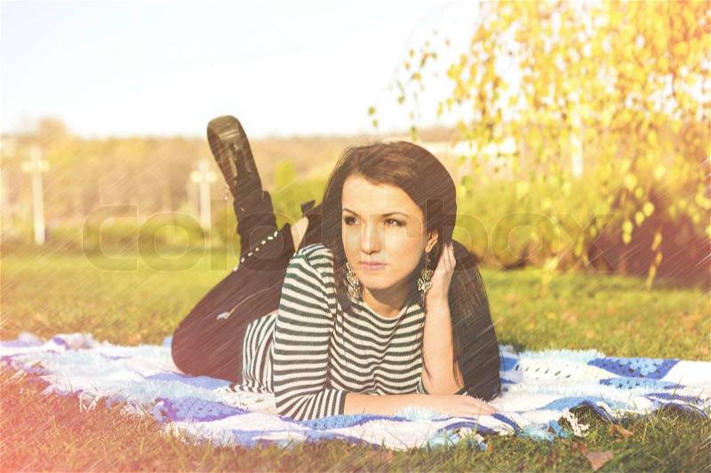 Young woman laying down on the ground in autumn park, stock photo