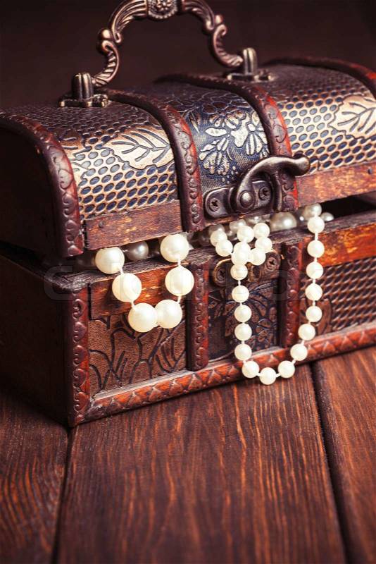 Old treasure chest with pearl necklaces standing on wooden table, stock photo