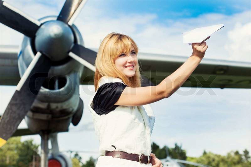 Beautiful woman holding paper plane against real plane, stock photo