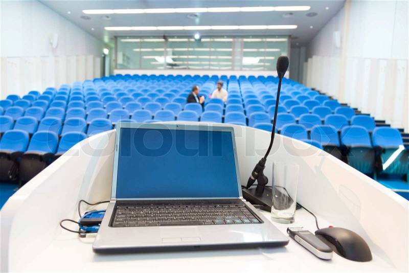 Laptop and microphone on the rostrum in conference hall with blue velvet chairs, stock photo