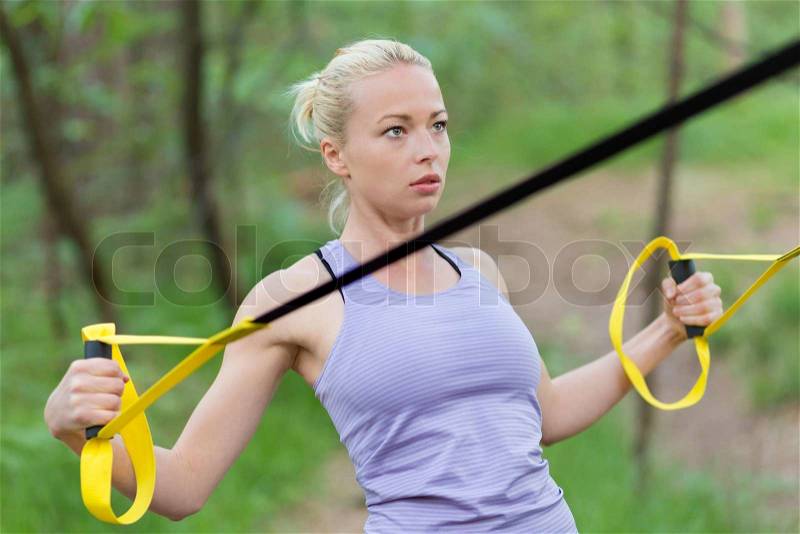 Young attractive woman does suspension training with fitness straps outdoors in the nature, stock photo