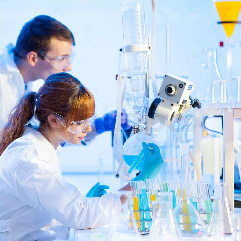 Chemical laboratory scene: attractive young PhD student and her post doctoral supervisor scientist observing the blue indicator color shift after the solution destillation, stock photo