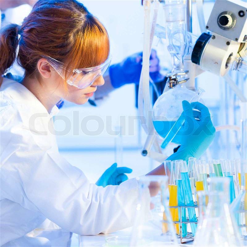 Chemical laboratory scene: attractive young PhD student scientist observing the blue indicator color shift after the solution destillation, stock photo