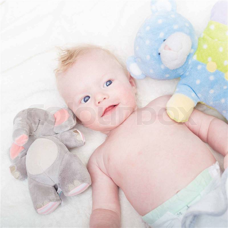 Cute blonde little baby boy with blue eyes with his favorite plush teddy bear and elephant toys, stock photo