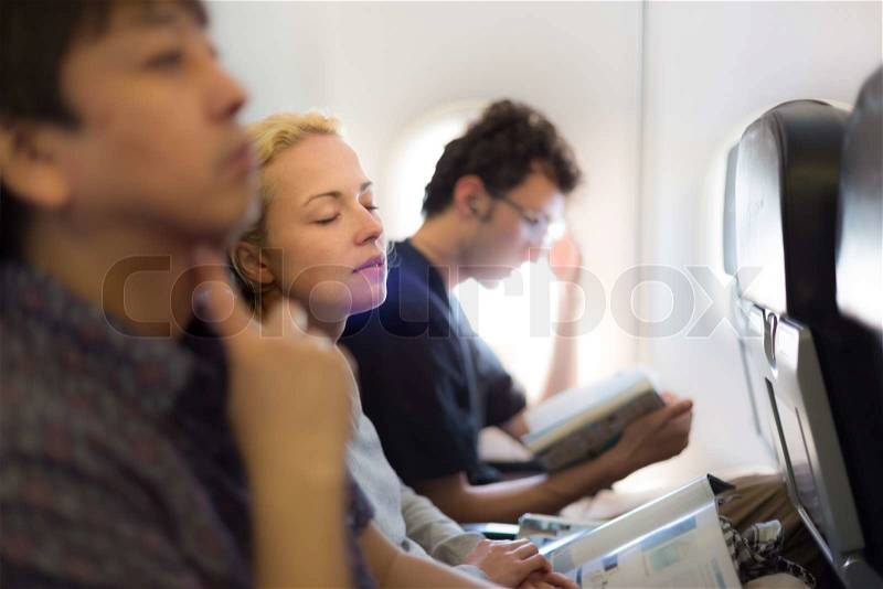 People flying by plane. Interior of airplane with passengers killing time on their seats, stock photo