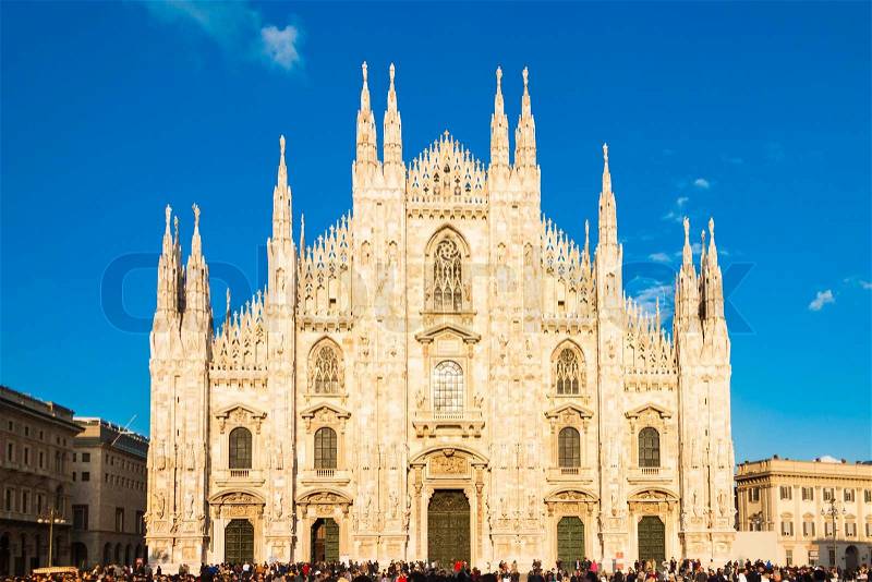 Milan Cathedral (Duomo di Milano) is the gothic cathedral church of Milan, Italy. Shot in the dusk from the square ful of people, stock photo