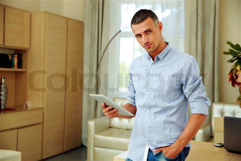 Handsome man standing with tablet computer at home, stock photo