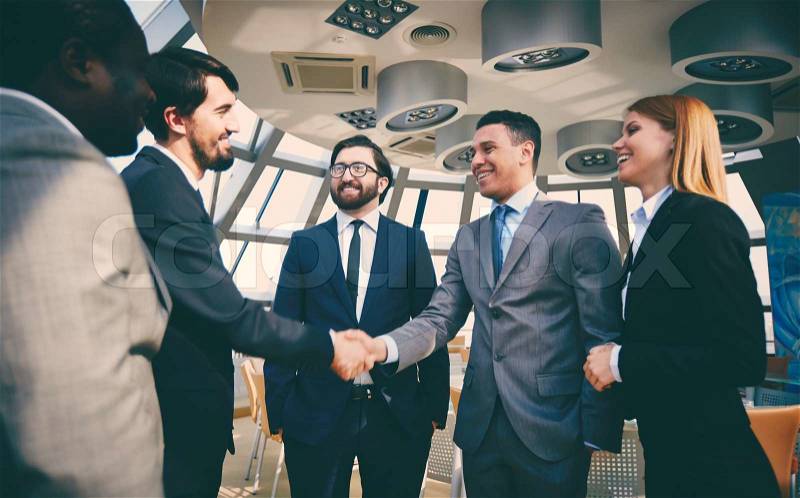 Group of business people looking at their colleagues handshaking after striking grand deal, stock photo