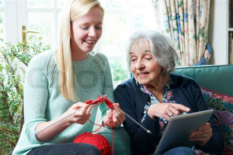 Grandmother With Digital Tablet Showing Granddaughter How To Knit, stock photo