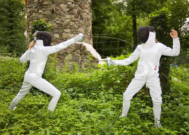 Two teenage girls practice fencing in the middle of the forest, stock photo