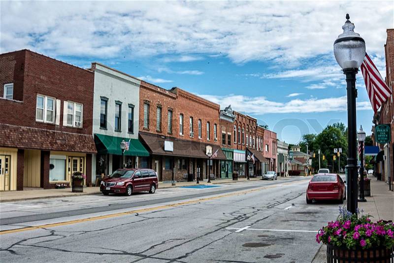 A photo of a typical small town main street in the United States of America. Features old brick buildings with specialty shops and restaurants. Decorated with spring flowers and American flags, stock photo