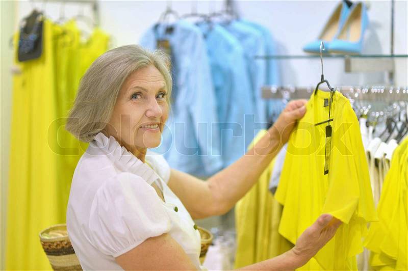 Smiling old lady choosing dress in store, stock photo