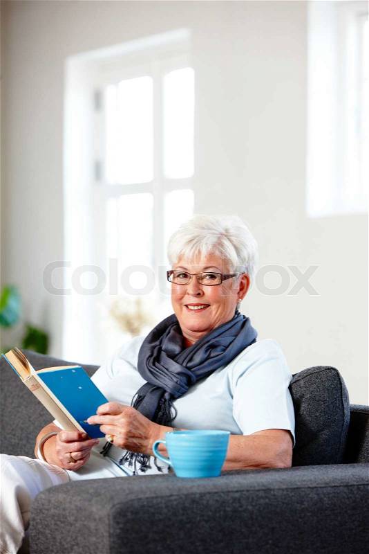 An elderly woman enjoying a cup of hot tea and a good book, stock photo