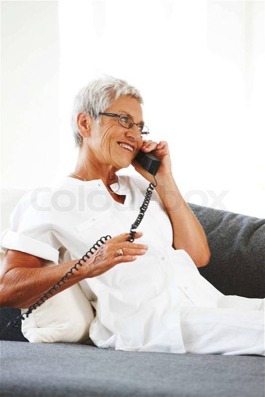An elderly woman on the sofa and sitting talking on the phone, stock photo