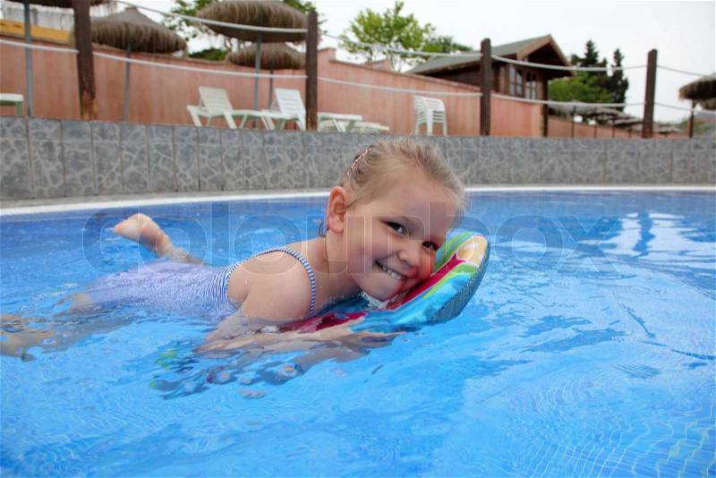Funny little girl swims in a pool with a small bodyboard, stock photo