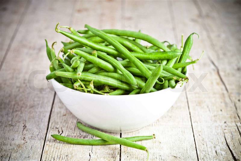 Green string beans in a bowl on rustic wooden table, stock photo