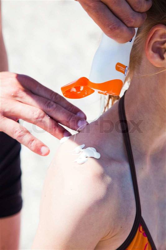 A man putting sunblock lotion on a girl's back, stock photo
