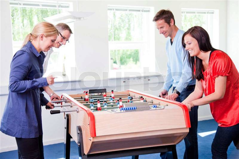 4 colleagues playing tabletop football in the break room of their office. Business people having fun i the break/ recreation room, stock photo