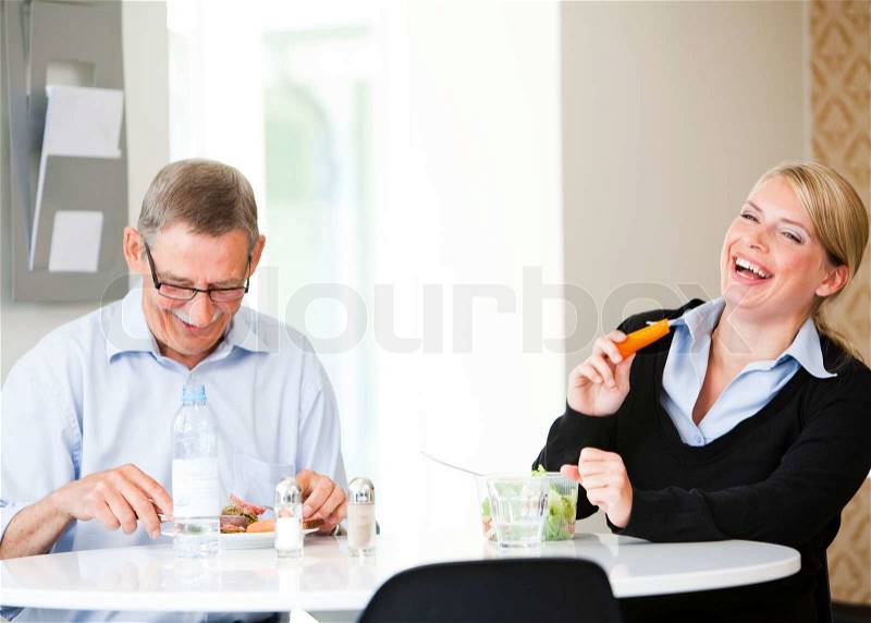 Two colleagues sitting in the break room, having lunch and laughing. Business people having lunch/ lunch break, stock photo
