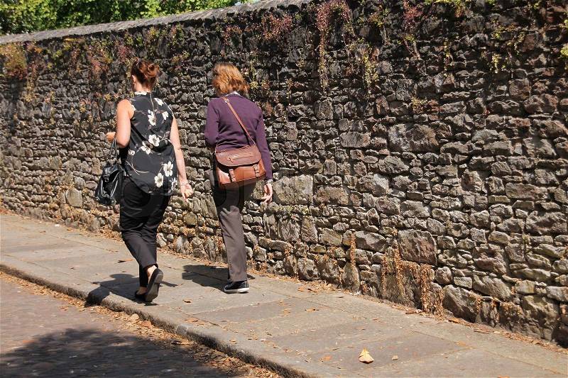 The two ladies going to their job along the wall at the foot path in summertime, stock photo
