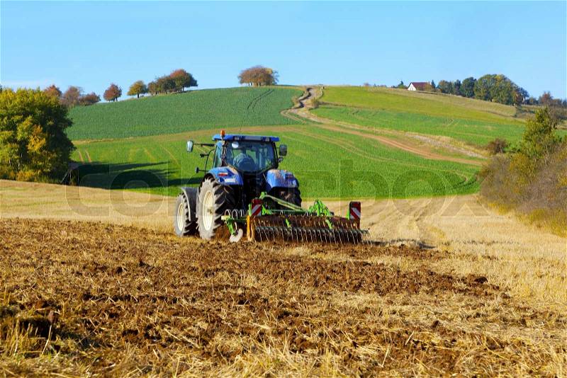 Farm tractor on the field working, plowing land, stock photo