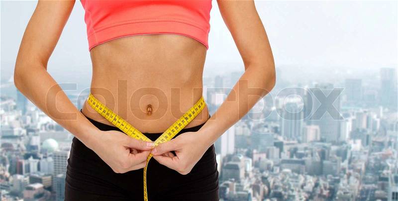 Diet, sport, fitness and heath concept - close up of female hands measuring waist with measuring tape, stock photo