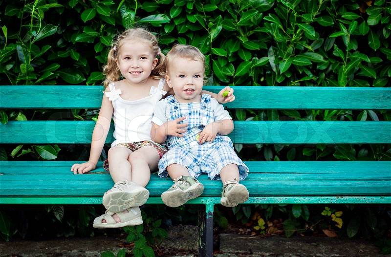Funny little children brother and sister sitting on bench, stock photo