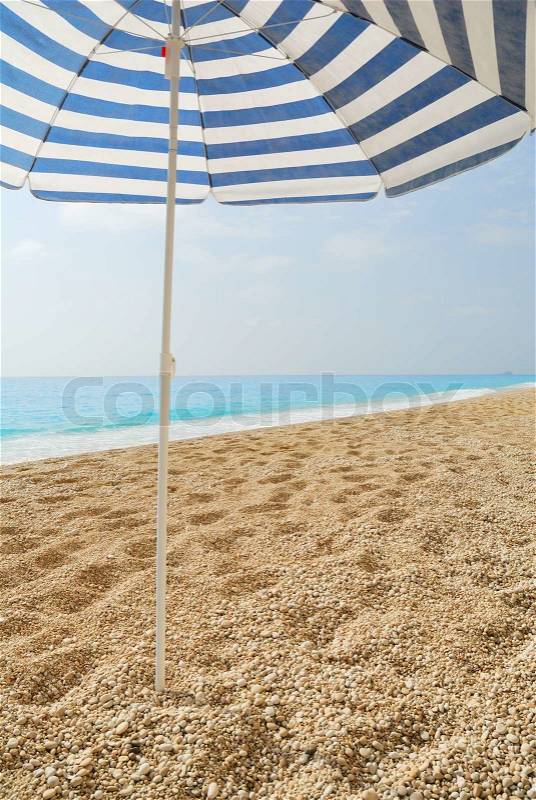 Sun umbrella stuck in a pebble beach with blue sea, stock photo