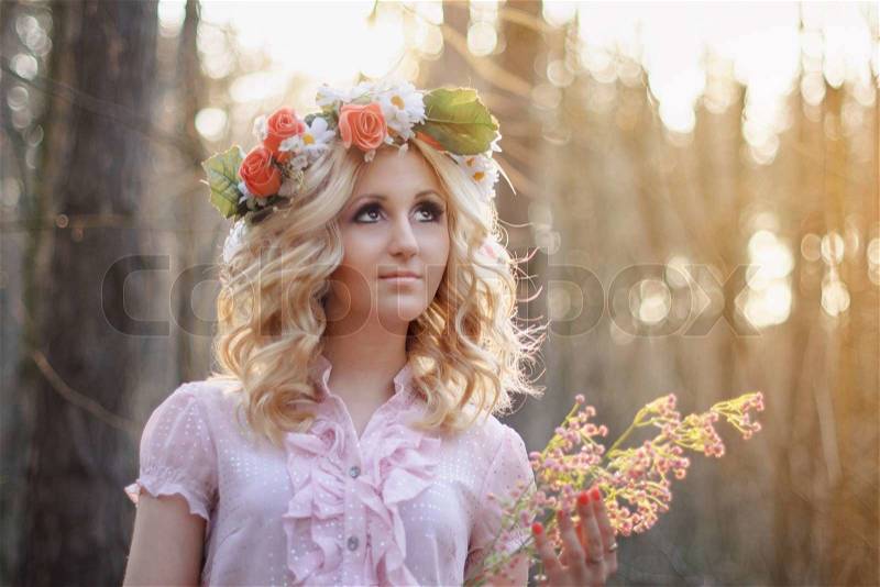 Pretty blonde girl in a pink dress and with flower wreath in the park, stock photo