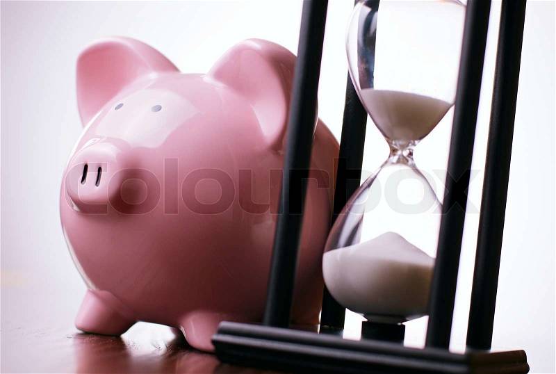 Close-up of a pink porcelain piggy bank with a vintage hourglass behind, concept of saving money and passing time, stock photo