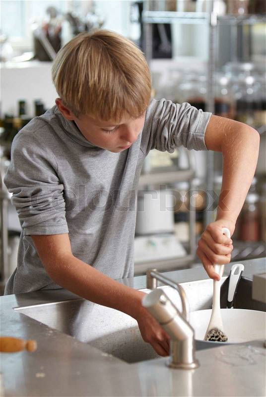 A caucasian boy washing dishes in the kitchen sink, stock photo